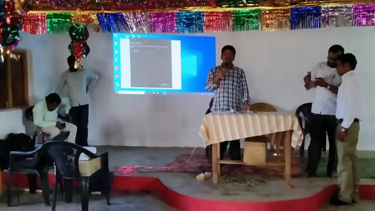speaker and 4 other men at front of a public meeting